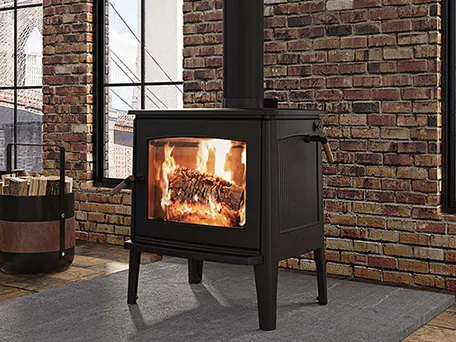 Black wood-burning stove with a roaring fire, set against a brick wall in a modern loft.