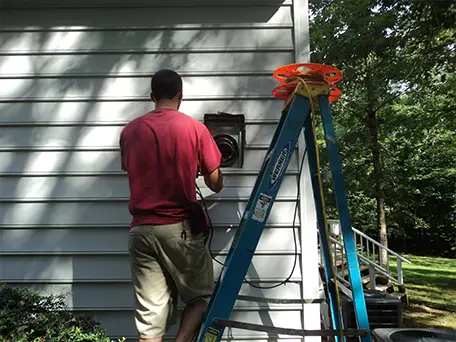 Technician cleaning fireplace vent on house exterior using ladder.