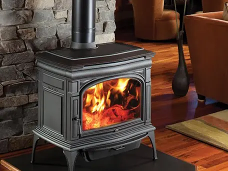 Cast iron wood burning stove with a roaring fire, installed in a stone fireplace.