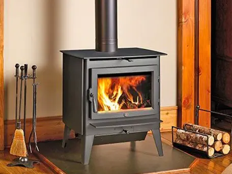 A freestanding wood-burning stove with a roaring fire, set on a hearth in a rustic living room.